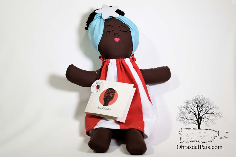 Muñeca de Teresa Meléndez vestida con los colores de la bandera de Puerto Rico y acompañada por un pequeño libro