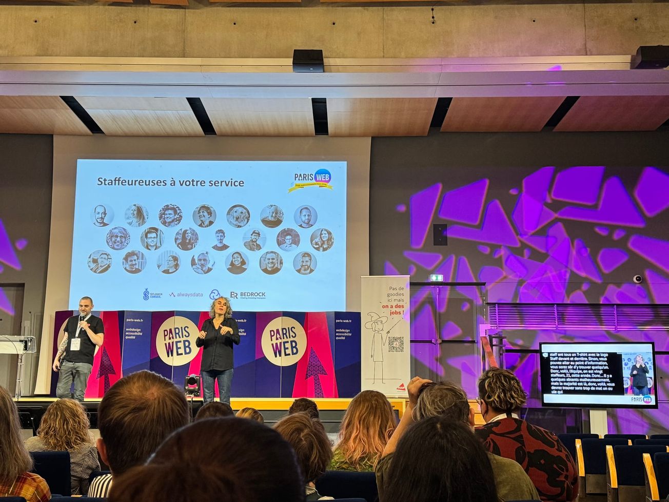 Un écran présente les photos des "Staffeureuses à votre service". Sur la droite de la scène on voit un écran affichant la retranscription en vélotypie et l'interprète LSF.