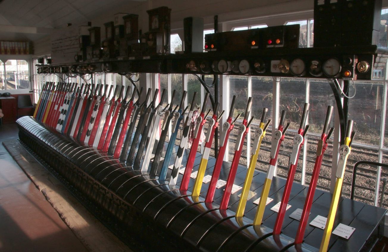 Pupitre d’un poste d’aiguillage ferroviaire : une rangée de leviers rouges, jaunes et bleus, numérotés, face aux voies