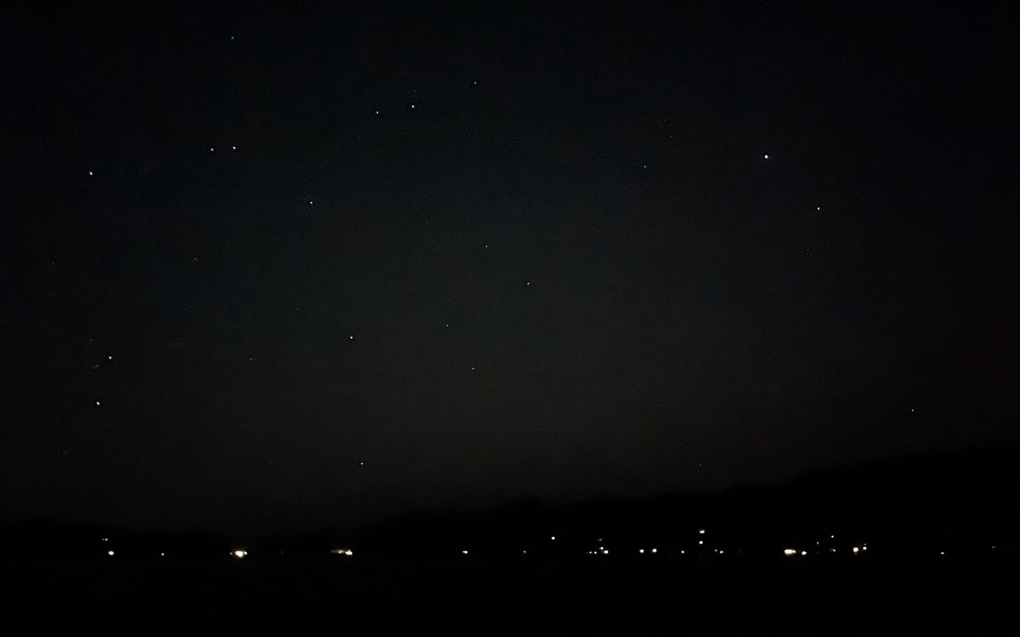 A dark evening sky, with some scattered stars visible, but no moon.