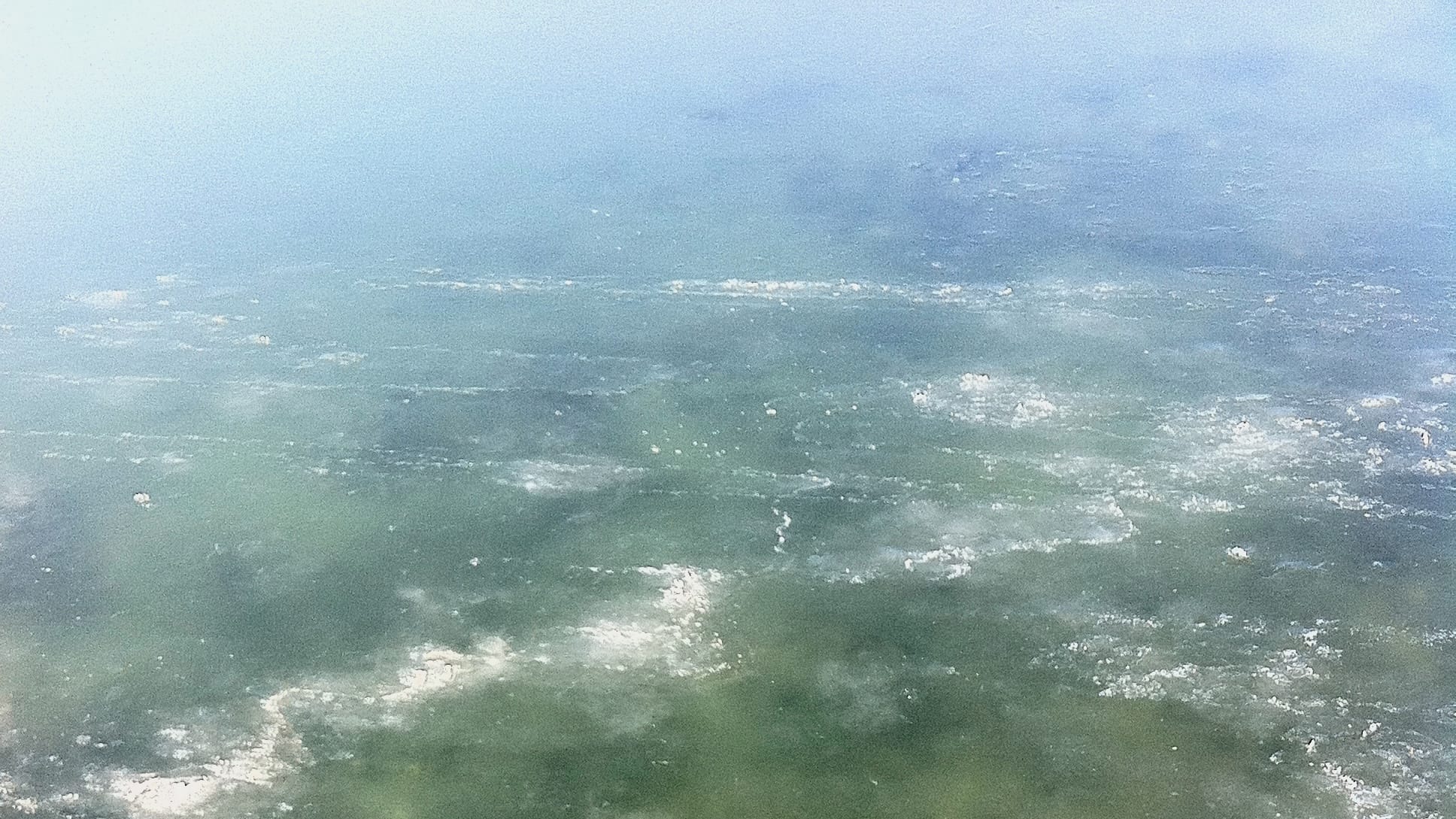 A very thin sheet of ice over a shallow body of salt water. Nearer to shore, the ice breaks and one can see the rocks at the bottom of the water.