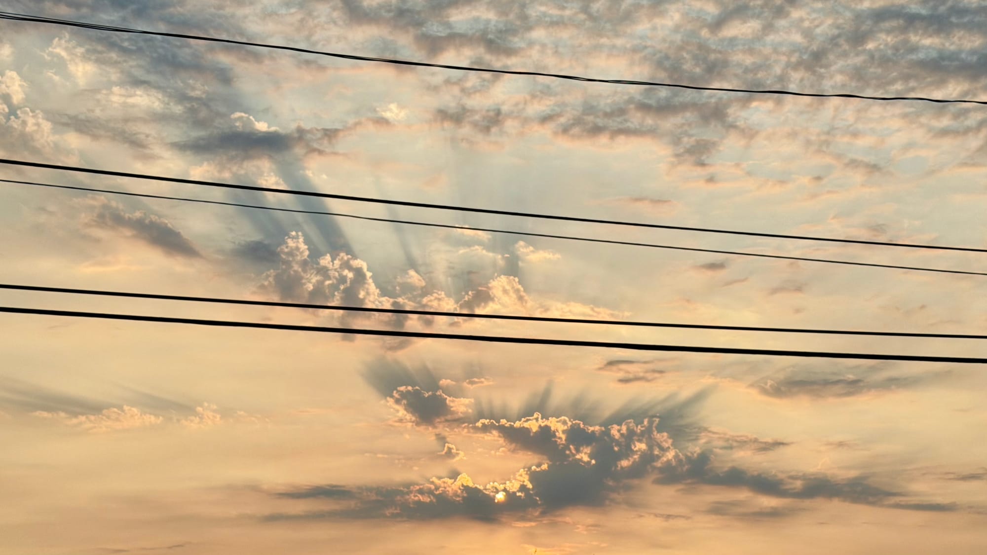 Sunset shadowing beyond clouds in a kinda grimy wildfire sky. Power lines visible at the forefront.