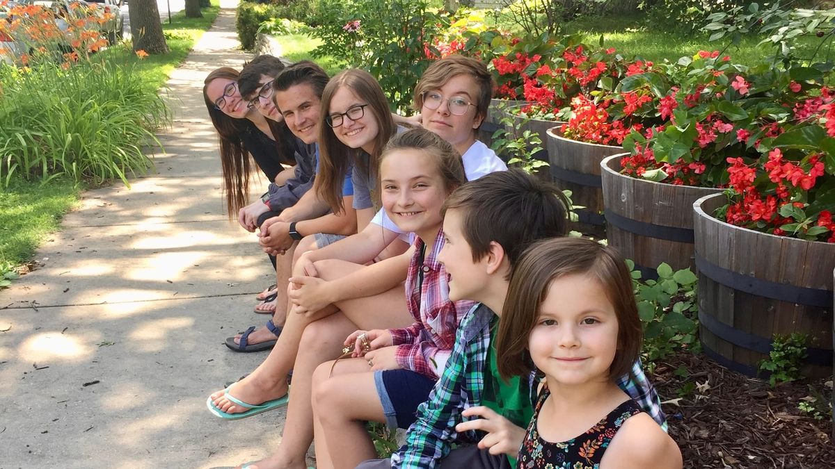 The eight Richert children sit on a stone-walled flowerbed in front of their former home in Rockford, Illinois. (Photo by Amy J. Richert)