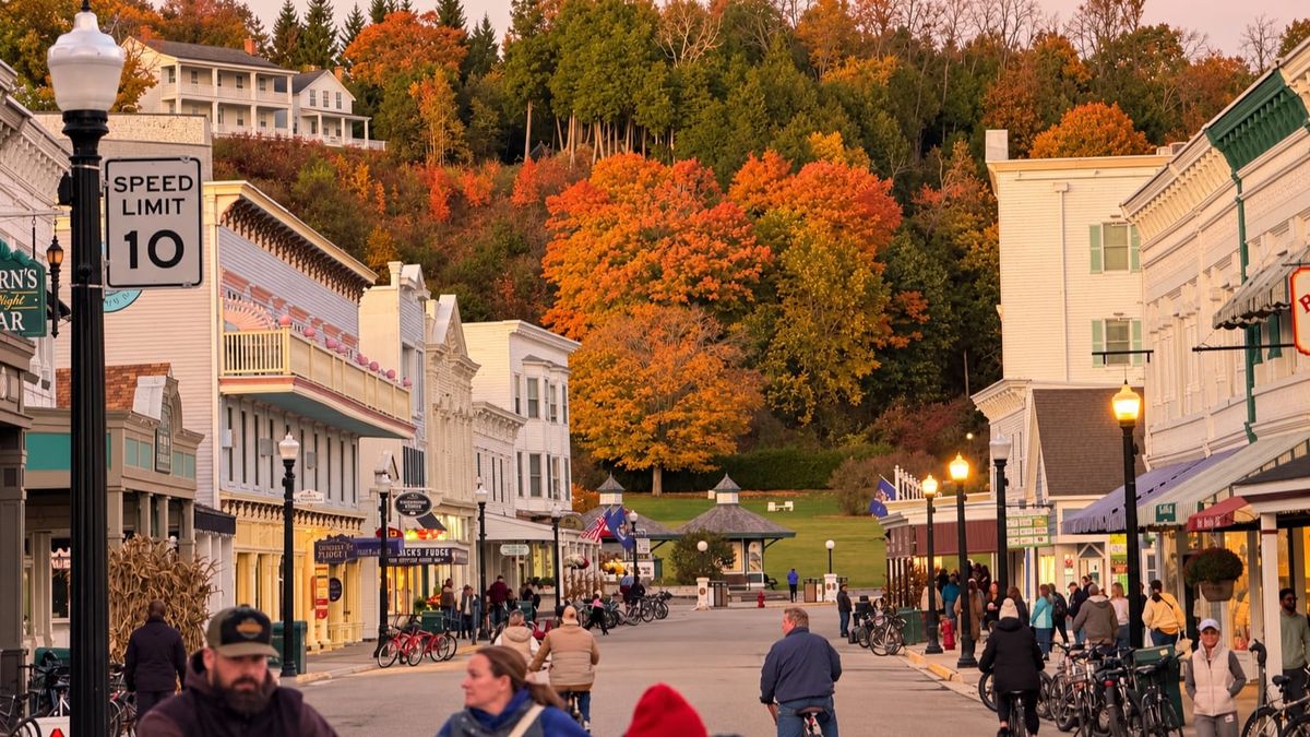 Autumn foliage rises above the storefronts on Mackinac Island’s Main Street, as people walk and cycle beneath glowing streetlamps. (Photo by Scott P. Richert)