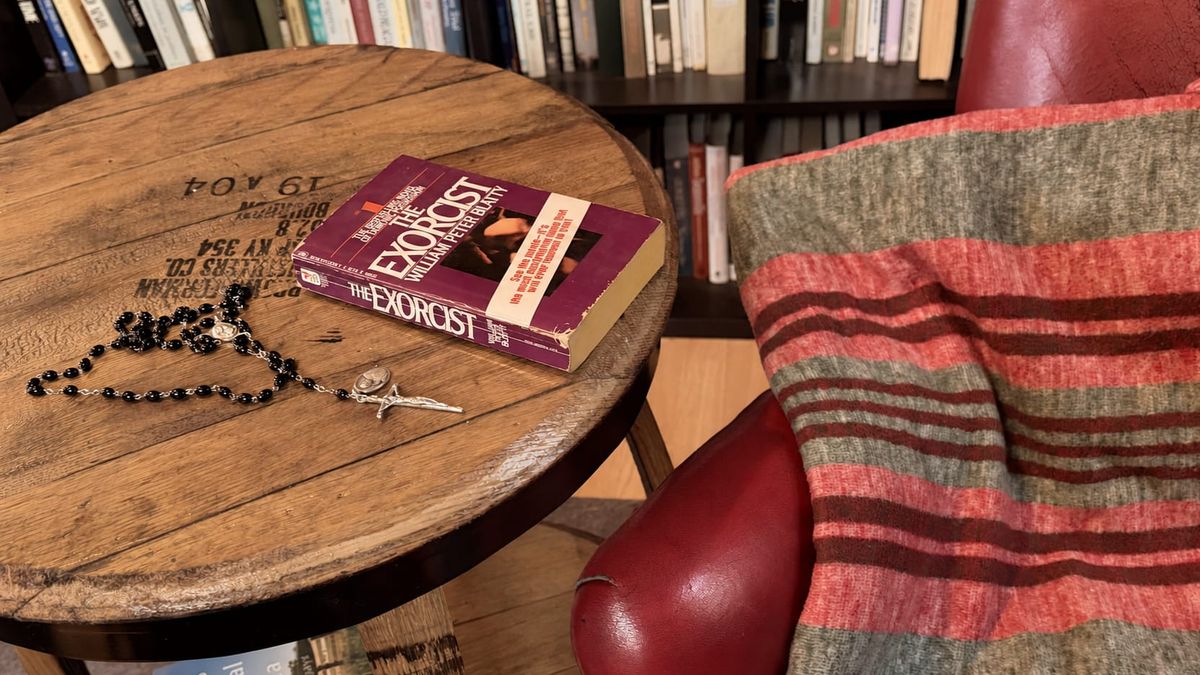 The author's copy of The Exorcist and a black rosary rest on a wooden table beside a red leather chair draped with a striped blanket. (Photo by Scott P. Richert)