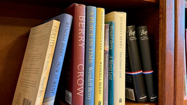 A number of Wendell Berry’s novels and collections of short stories sit on a red wooden bookshelf. (Photo by Scott P. Richert)