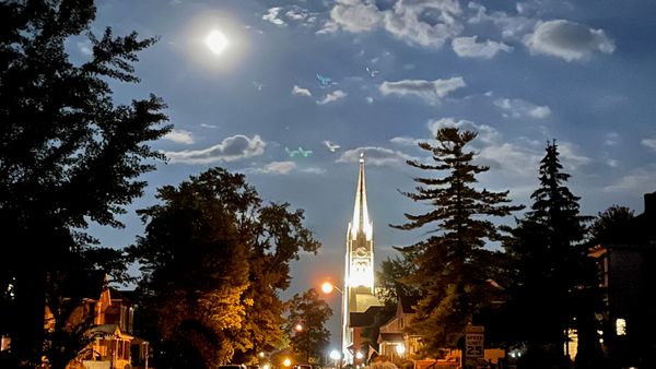 A moonlit residential street in Huntington, Indiana, leads toward an illuminated church steeple. Photo by Scott P. Richert.