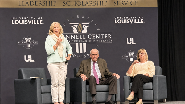 Wendell Berry sits between two women on a stage at the McConnell Center at the University of Louisville. (AI-assisted restoration of a photograph by Scott P. Richert.)