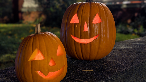 Two glowing jack-o'-lanterns sit on a stone wall in front of a porch. (Photo by Scott P. Richert)