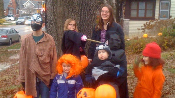 The Richert children in Halloween costumes pose beside a tree with orange pumpkin candy buckets. (Photo by Scott P. Richert)