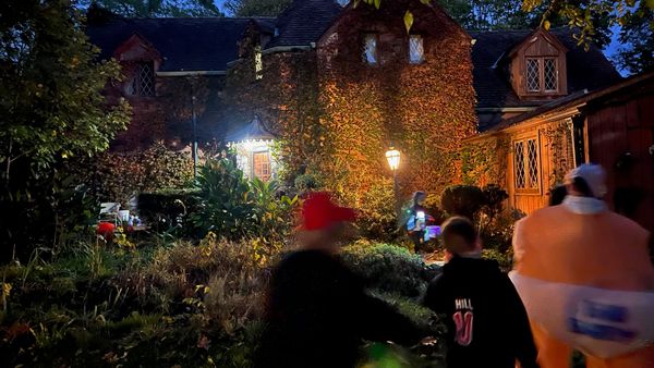 Trick-or-treaters approach an ivy-covered house illuminated by warm porch and garden lights. (Photo by Scott P. Richert)