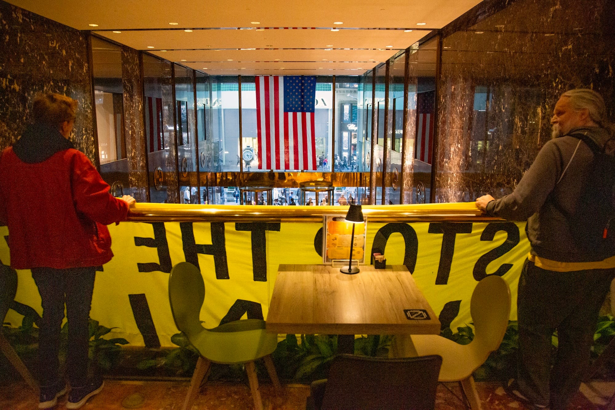 Activists on the balcony holding their banner, seen from behind. US flag in window in the background.