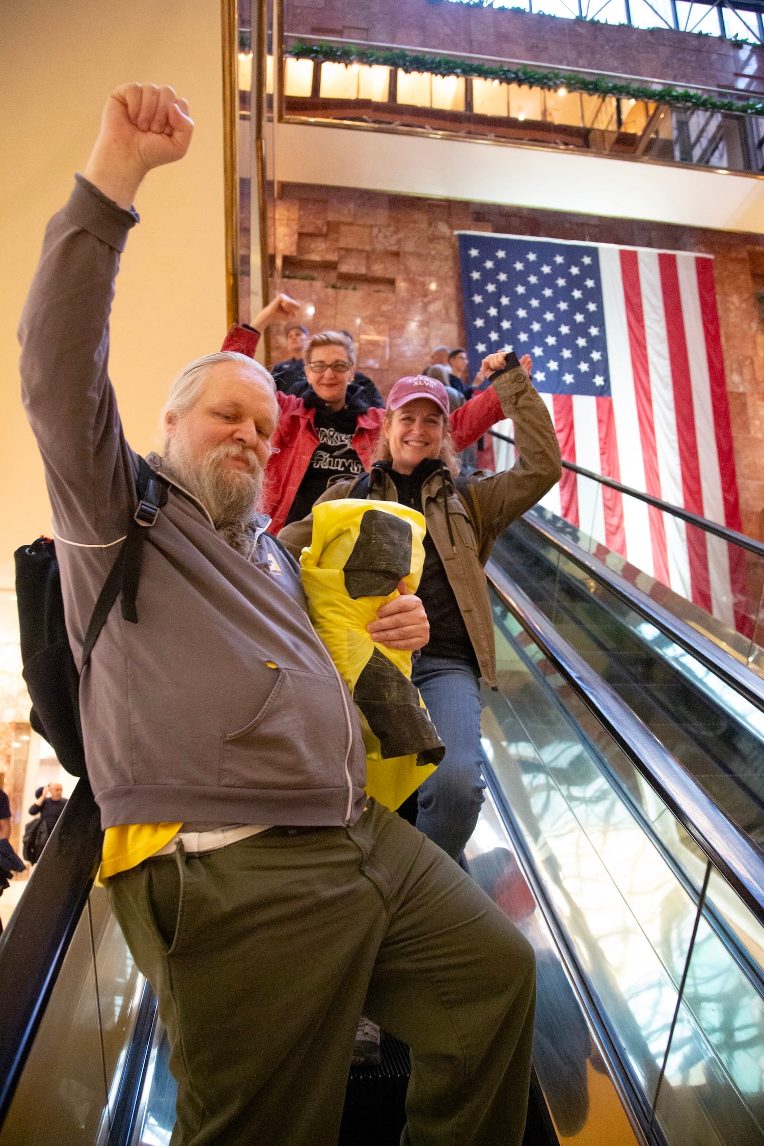 Protestors ride the escalator down to the ground floor after finishing their banner drop. Smiling, fists in the air.