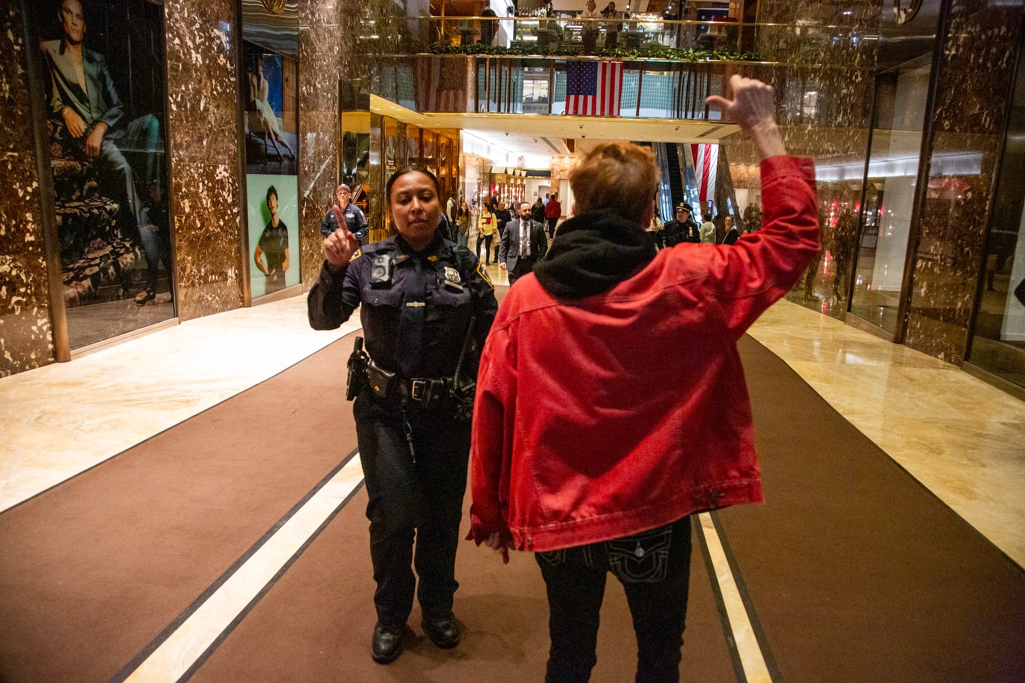 A police officer raises a finger at a protestor as the protestor turns to cheer to the crowd before exiting Trump Tower.