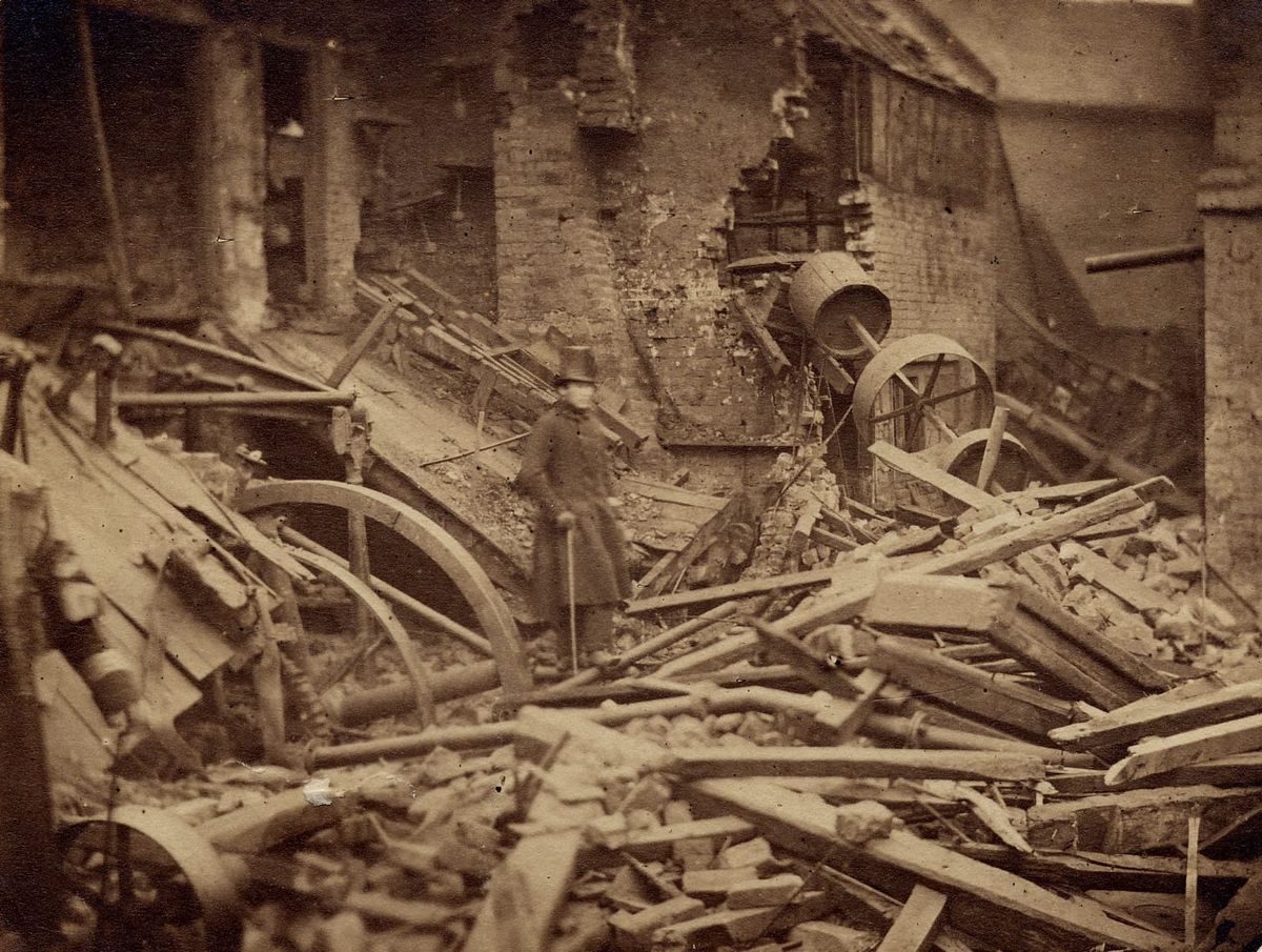 A man in a coat and top hat stands amid rubble after the steam boiler explosion in Wolverhampton, 1857.