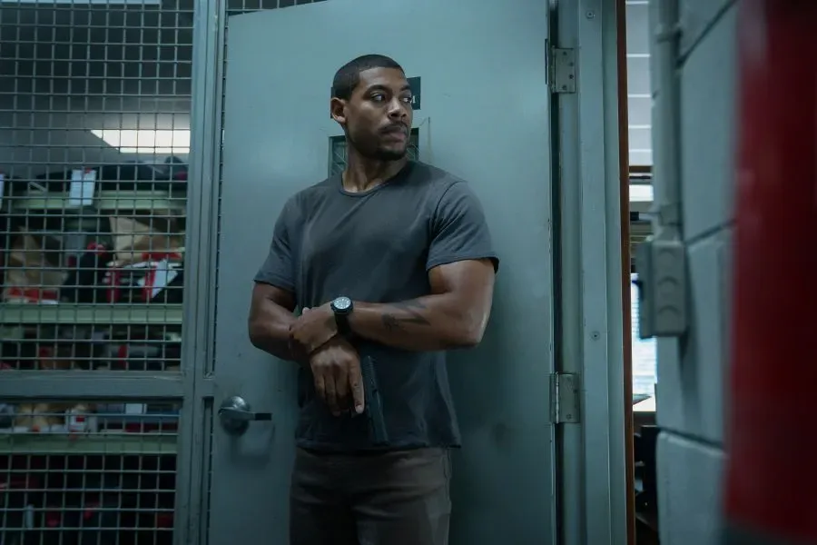 Aaron Pierre holding a gun and standing against a door in the film Rebel Ridge