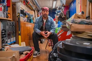 Vincent Grashaw sits in a crowded storage space surrounded by film canisters and looks at the camera.