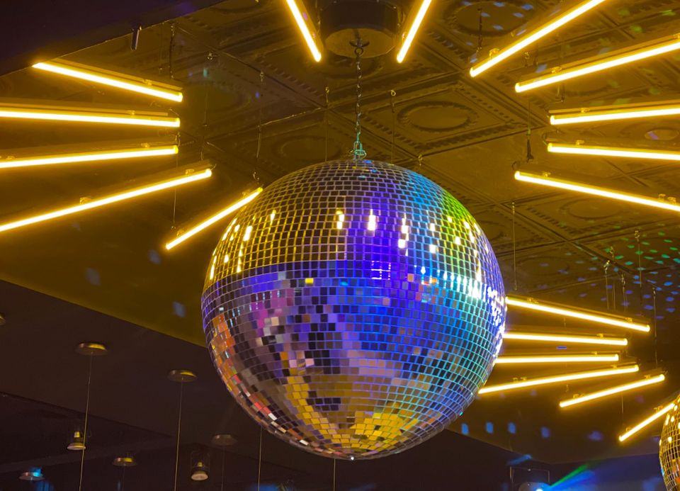 A disco ball reflecting the many neon lights surrounding it. 