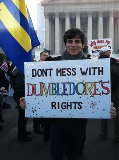  A man holding a rainbow sign reading “DON’T MESS WITH DUMBLEDORE’S RIGHTS.” He is at a protest. 