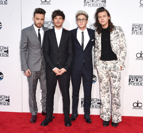  A photograph of Liam Payne, Louis Tomlinson, and Niall Horan all wearing relatively conservative suits. Harry Styles wears a flamboyant floral suit. 