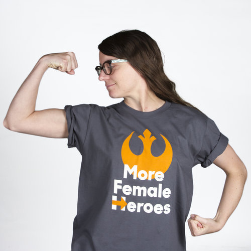  A woman flexing, wearing a t-shirt with the  Star Wars  Rebel Alliance sign and the phrase “More Female Heroes.” The “H” in “Heroes” is Hillary Clinton’s campaign insignia. 