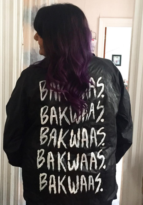  Preeti wears a black jacket with “BAKWAAS.” painted five times in white on the back. 