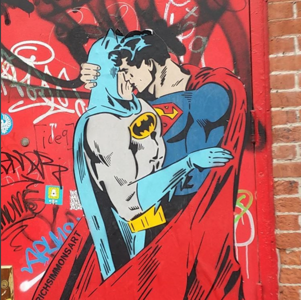  A mural, partially covered in graffiti, of Batman and Superman kissing. 