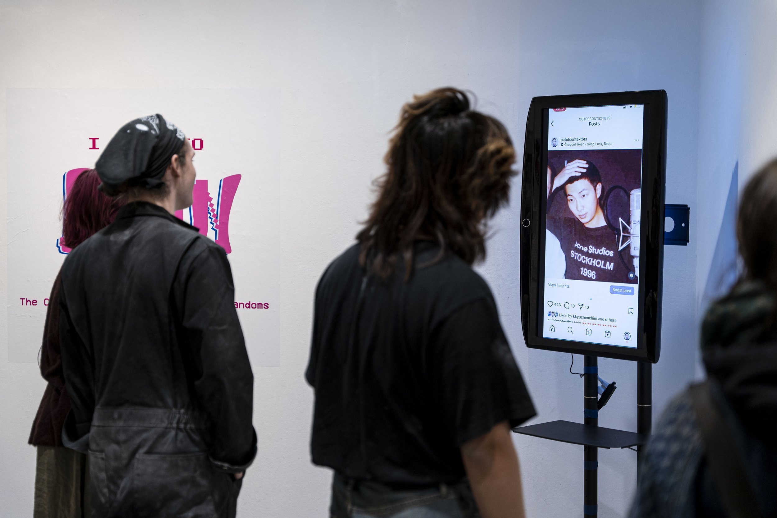 Exhibit viewers looking at a video instillation showing a meme from outofcontextbts on Instagram.