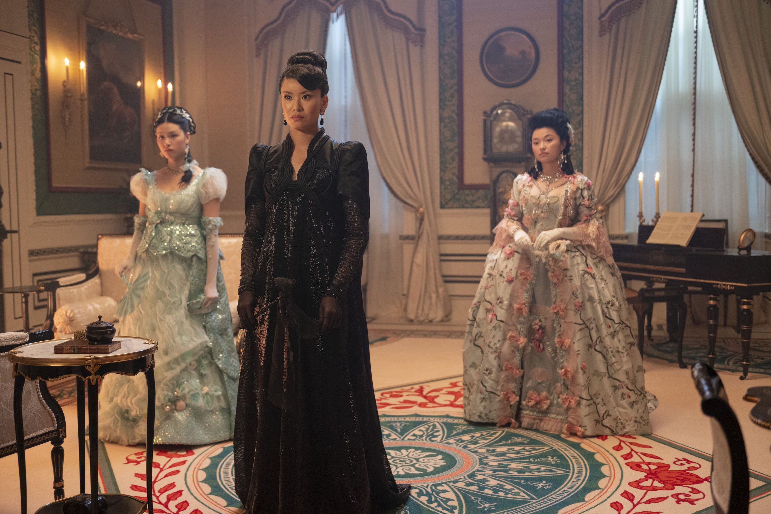 Promotional still featuring three members of Sophie's stepfamily in gowns, standing in a formal period room.