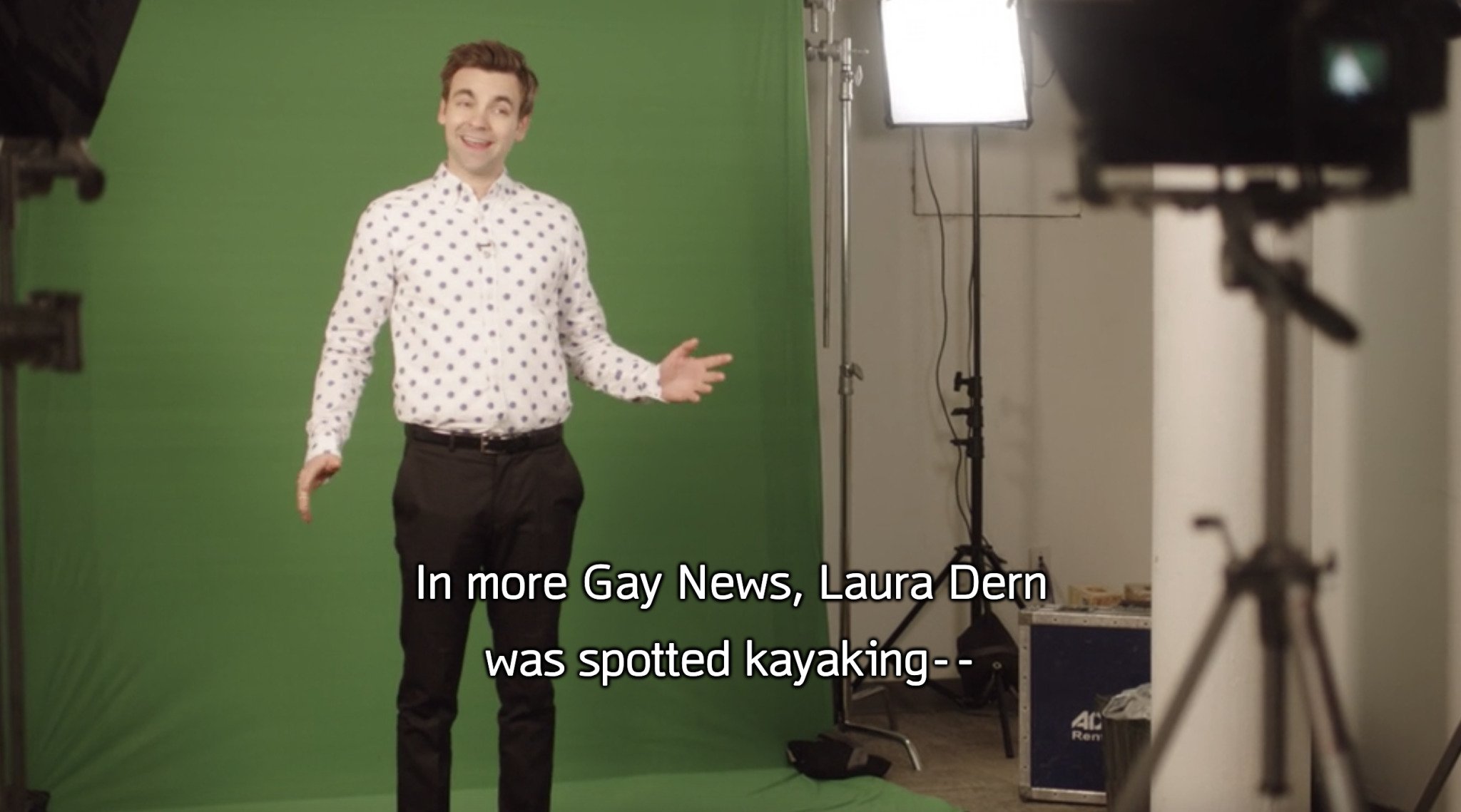 Screencap of Carey from The Other Two in front of a green screen. Subtitle reads: "In more Gay News, Laura Dern was spotted kayaking -- "
