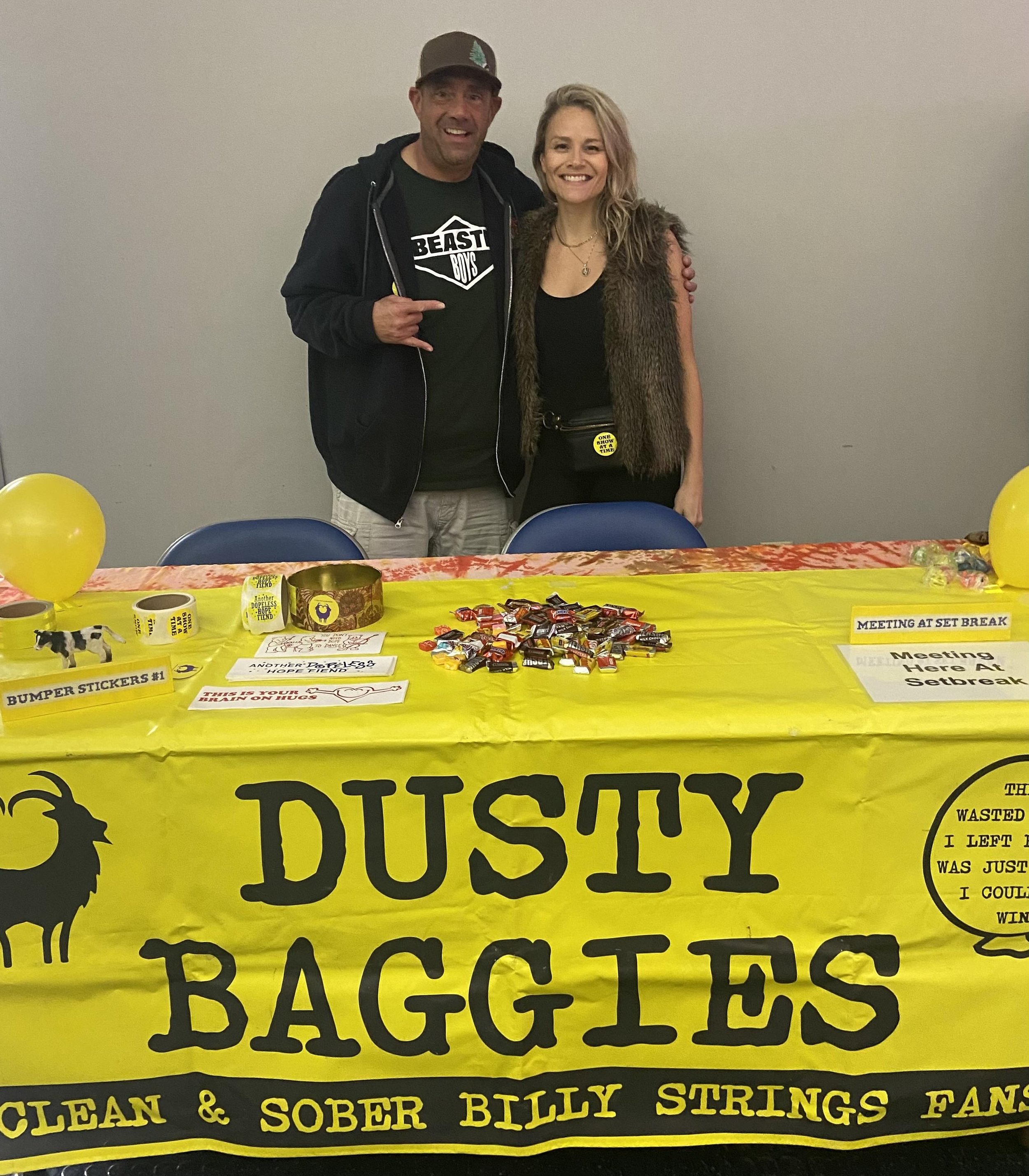 Photo of two people in front of a table with a sign that says Dusty Baggies.