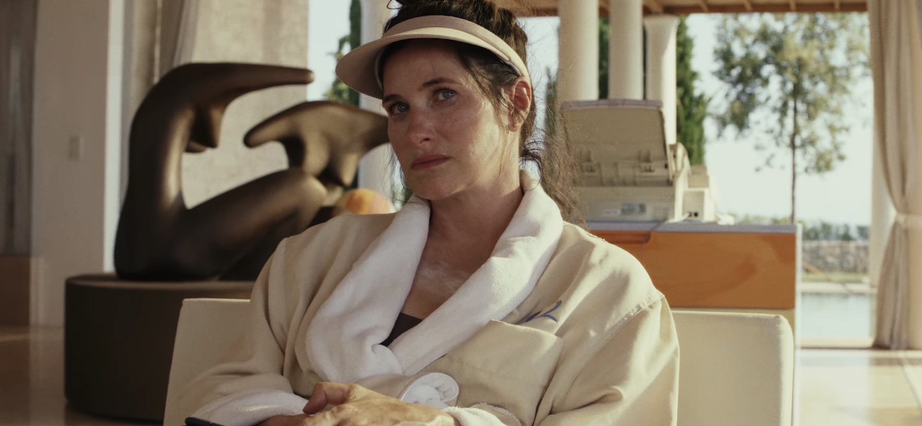Still from Glass Onion of Kathryn Hahn in a robe and visor (with messy eye makeup)