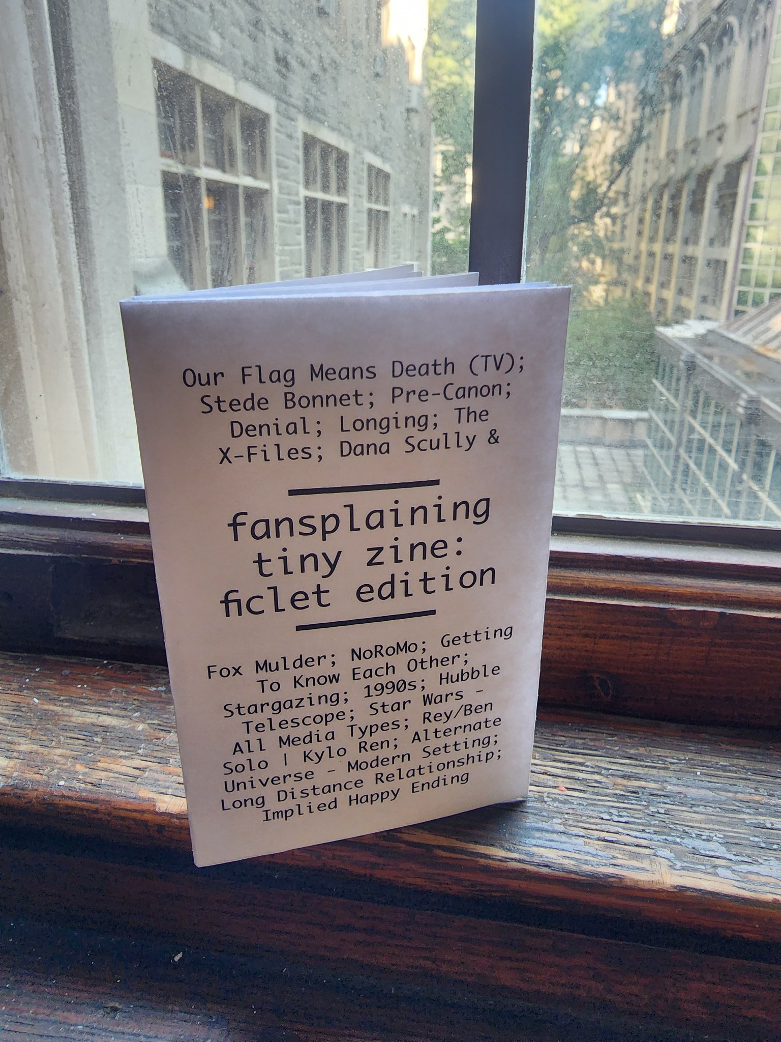 Photograph of the newest tiny zine stood up on a windowsill