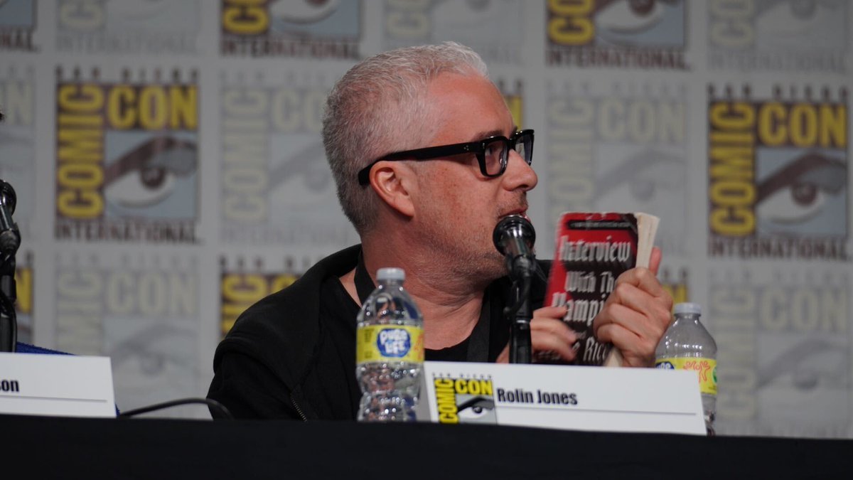 Image of Rolin Jones on a stage at SDCC holding a battered copy of IWTV