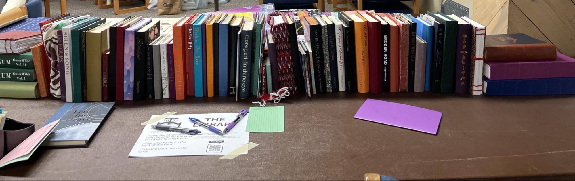 Long row of books on a table with a signup sheet and several pens