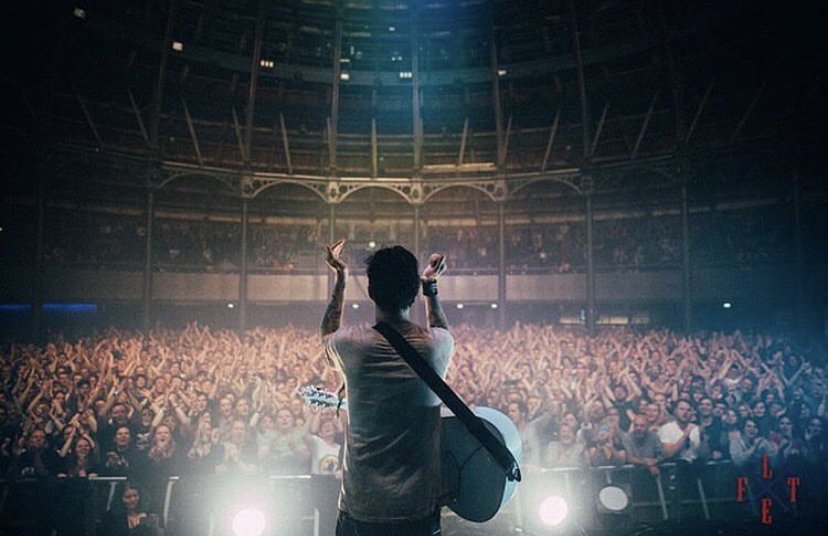 Photo of the back of a musician with a guitar facing a crowd of cheering people.