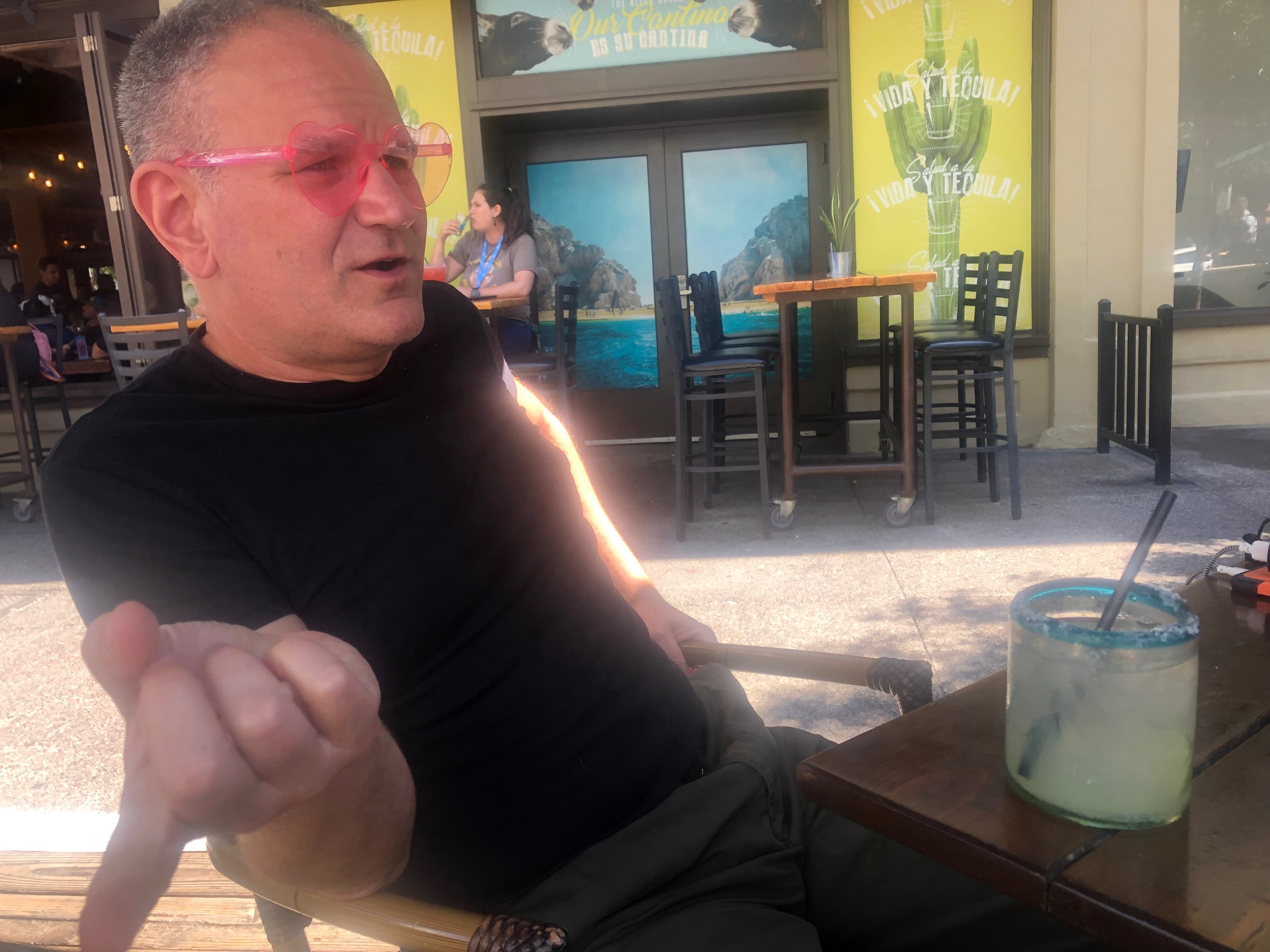 Photo of Javi in heart-shaped Barbie glasses sitting at an outdoor table