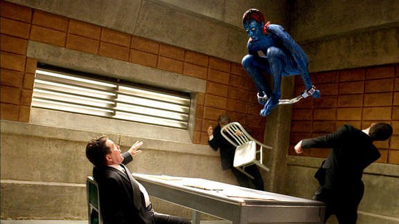 Still photograph of Mystique from the X-Men flying through the air while handcuffed, and the suited men who were interrogating her cowering in terror.