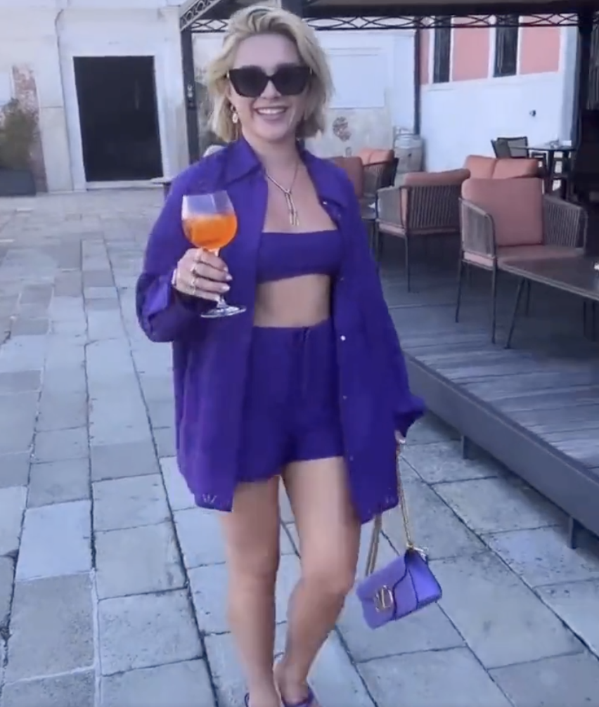 Photograph of Florence Pugh in an all-purple outfit, holding an Aperol Spritz
