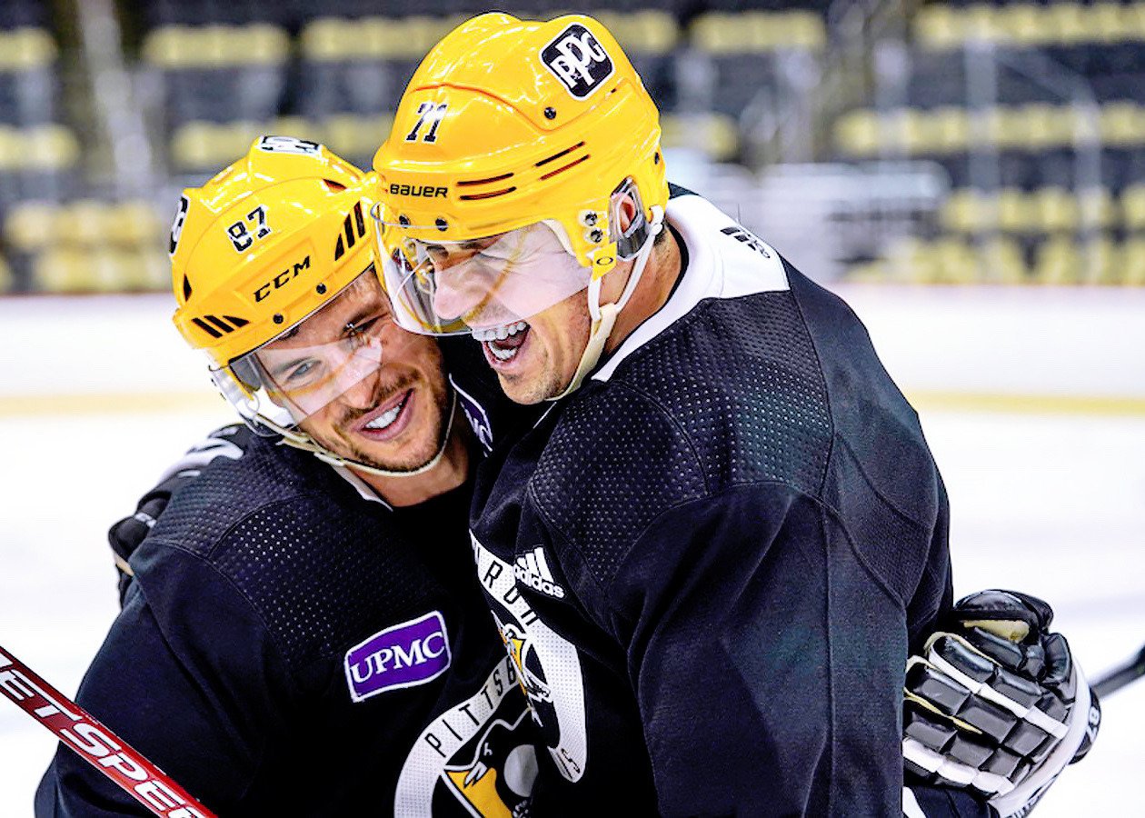 Photograph of Sidney Crosby and Evgeni Malkin from the Pittsburgh Penguins, in full uniforms and gear on the ice, hugging and grinning.