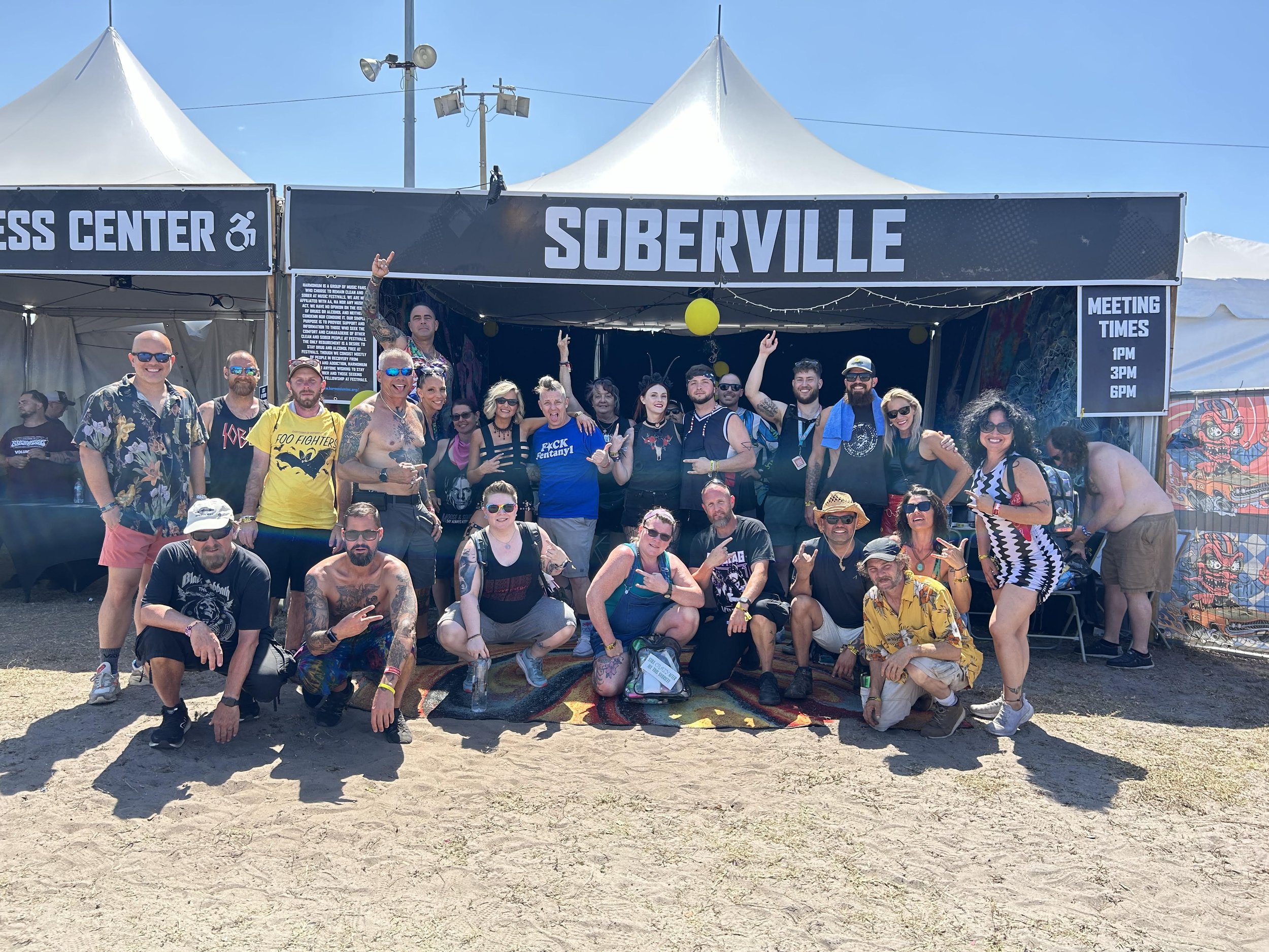Photograph of a festival tent labled "Soberville" with a large crowd of people posing in front of it