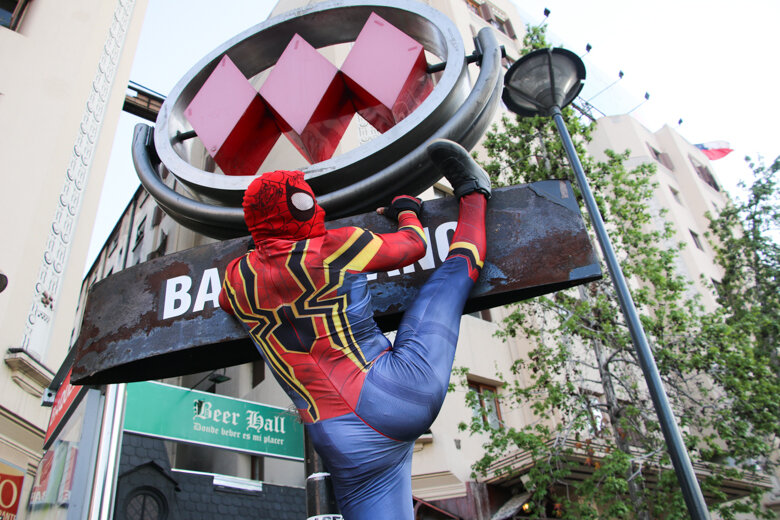 A Spider-Man cosplayer with a very defined butt on display climbs a sign.