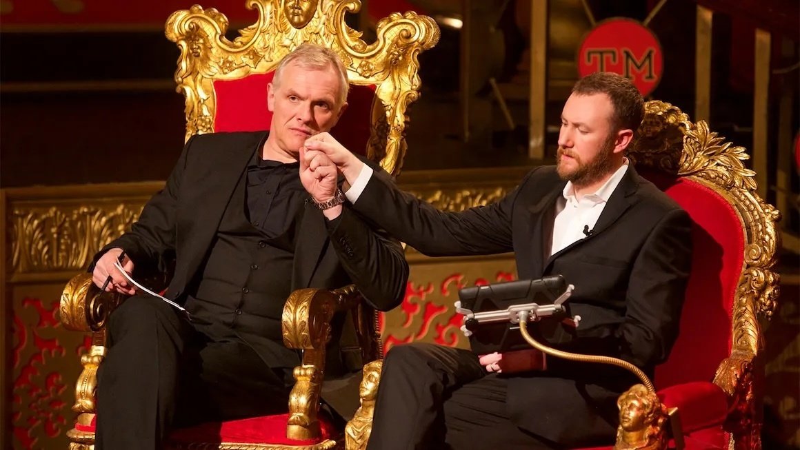 Image of Greg Davies and Alex Horne on Taskmaster, sitting on gold and yellow thrones, holding hands.
