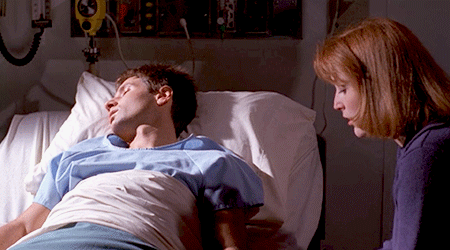 Animated gif of Mulder asleep in a hospital bed and Scully holding his hand.