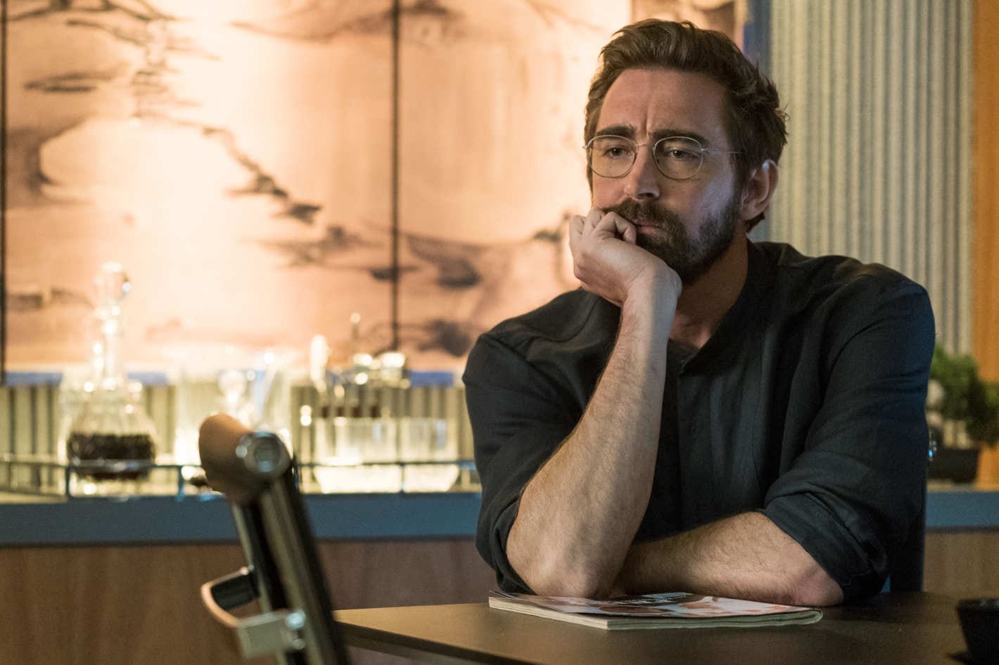 Image of Lee Pace as Joe sitting at a desk resting his hand on his chin.