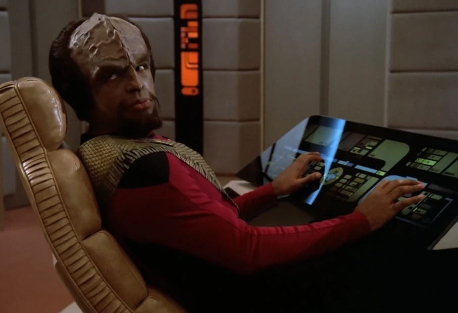 Image of Worf in his seat on the bridge of the Enterprise, hands on the controls.
