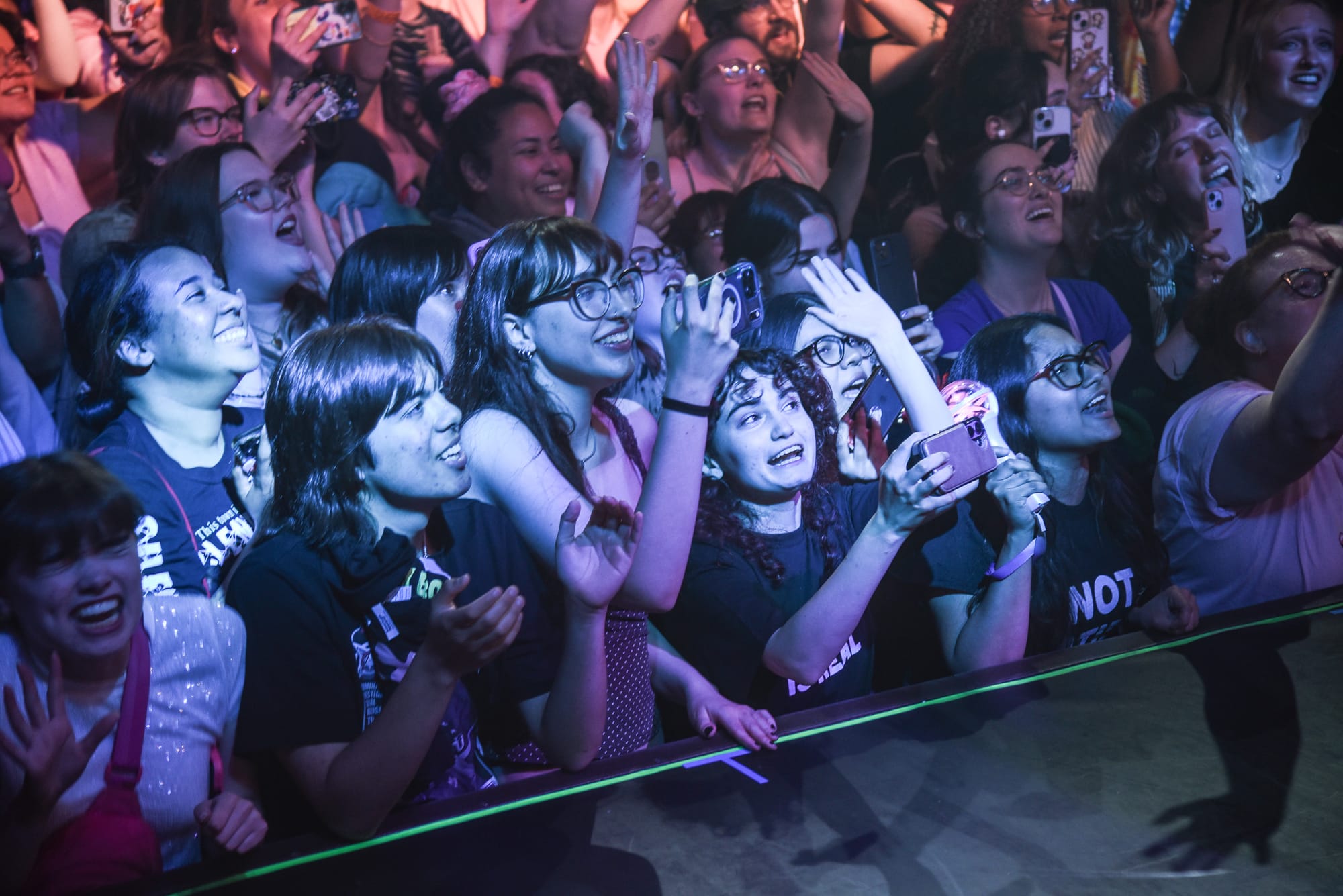 Photograph of a collection of screaming fans holding up their phones in the crowd of a show.