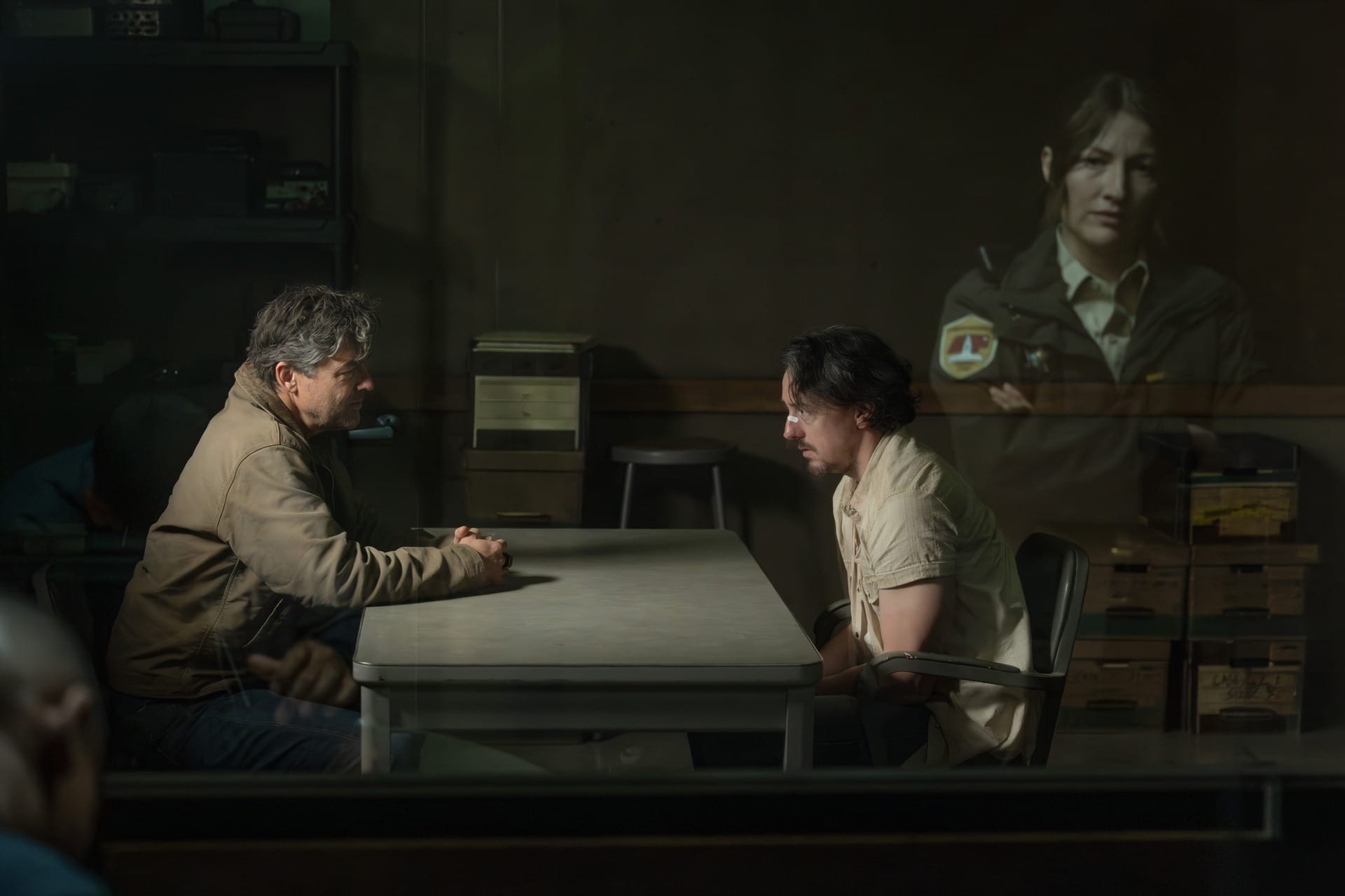 Production still featuring Hal and Waylon in an interrogation room, with the reflection of Kerry in the glass.