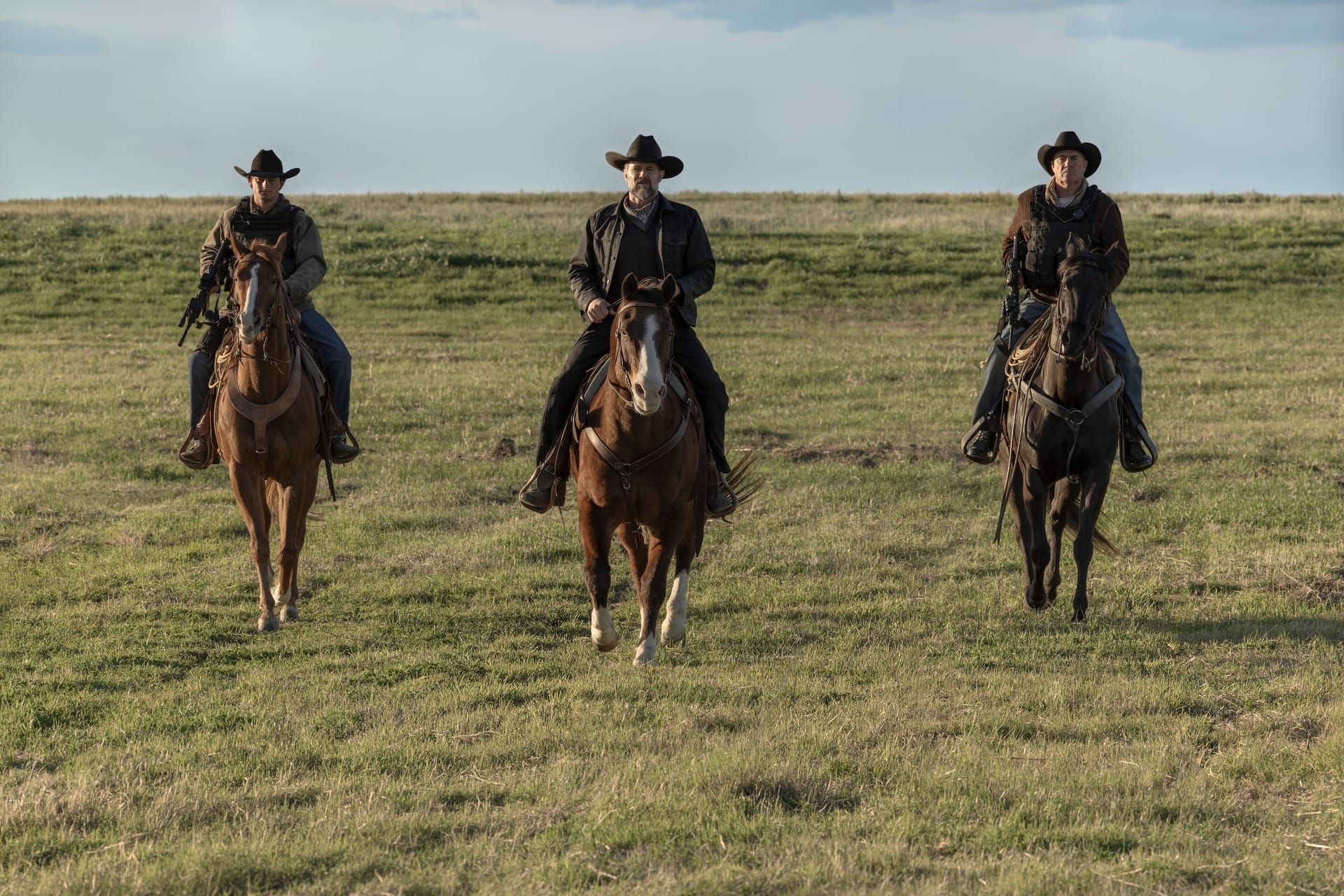 Production still featuring three men in cowboy hats riding horses.