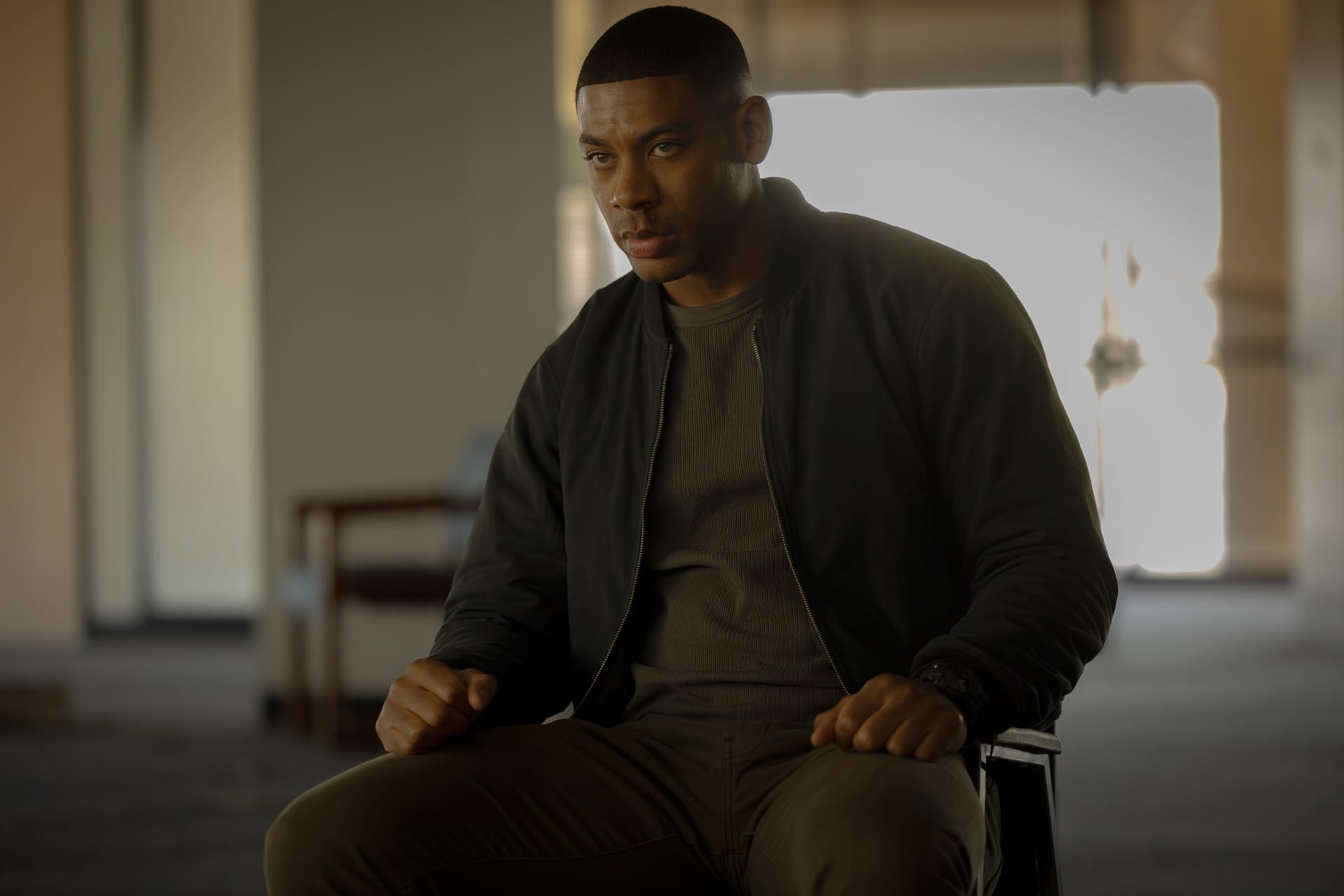 Production still featuring John sitting in a chair.